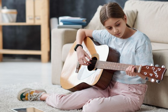 Una nena tocant la guitarra a la seva habitació